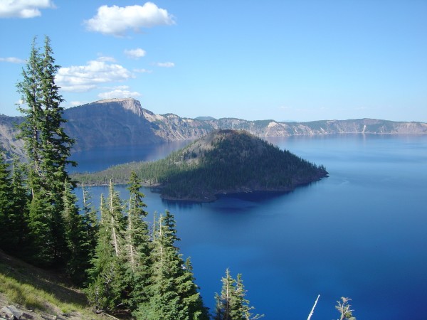 Spectacularly blue lake and sky with cinder cone rising in the center. trees in foreground.