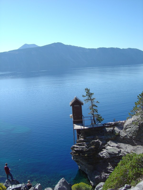 Small brown hut on platform on rocks above lake.