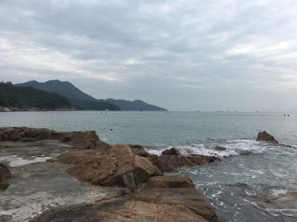 Lamma Island in Hong Kong. A volcanic rock jetty in the foreground, and a forested hilly shore.