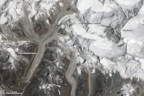 Satellite view of Mount Everest and the surrounding peaks. The summits are covered with bright white snow. The icy glaciers in the valleys between the peaks are a dirty grey colour, covered by debris weathered from the slopes above them.