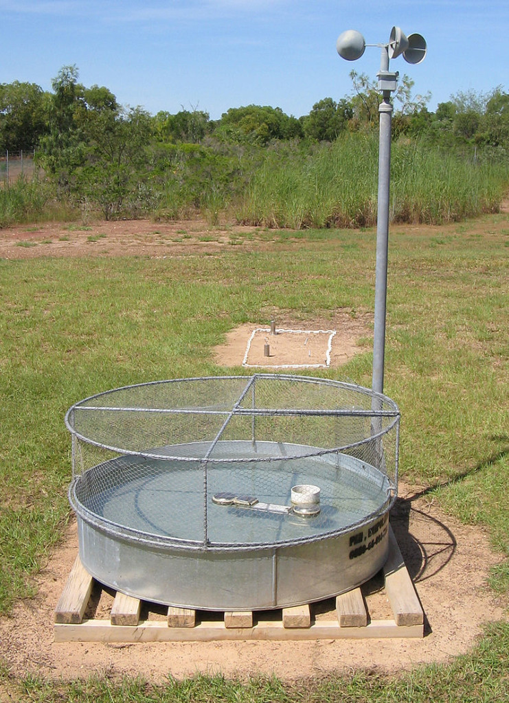 Metal pan filed with water with a fence over the top, on a pallet in a mowed area. 